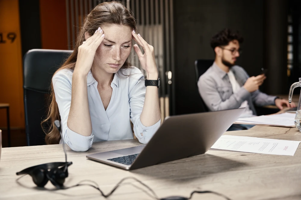Stressed woman at a laptop holding her head in an office