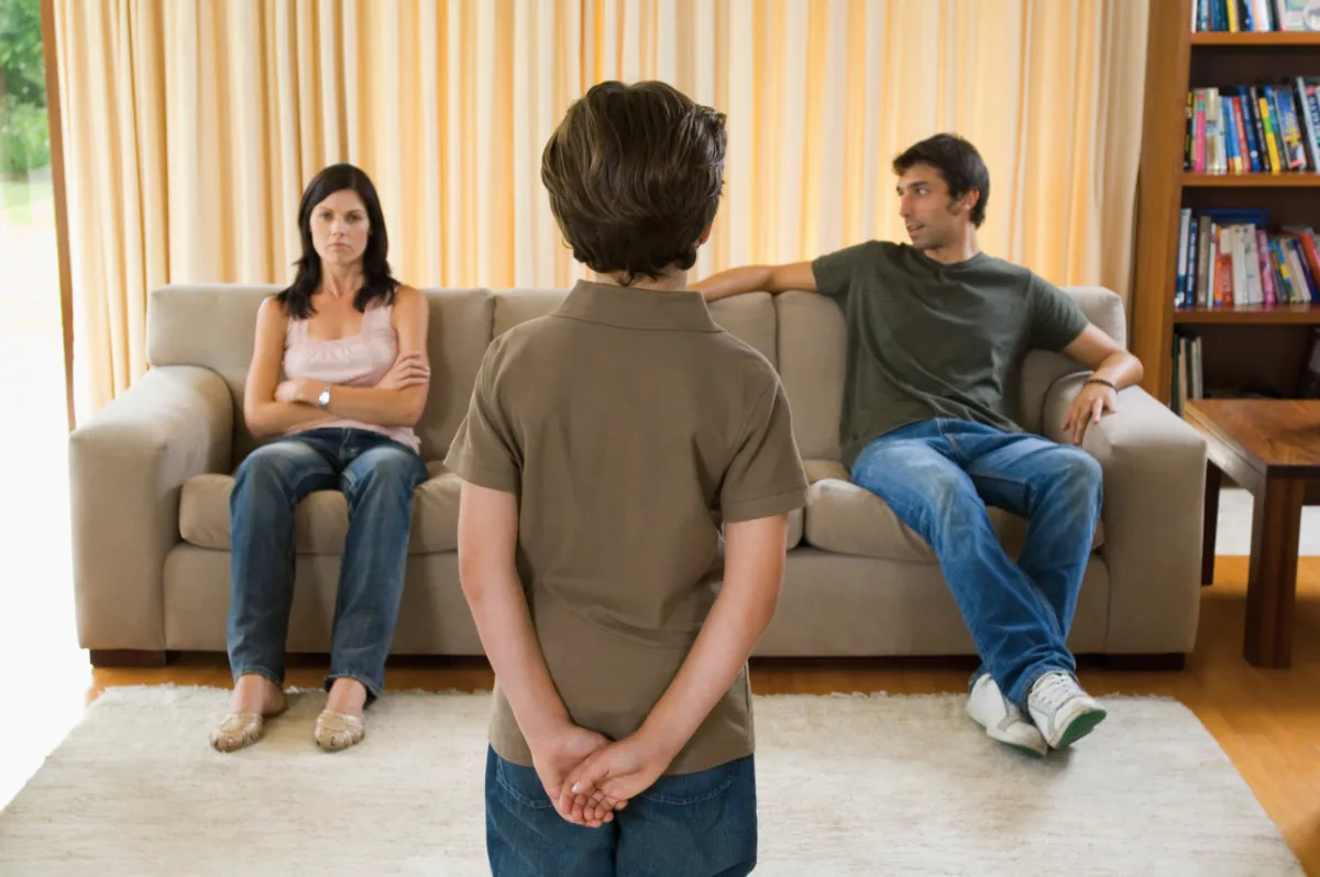 Young son standing in front of parents sitting apart on a couch, looking tense