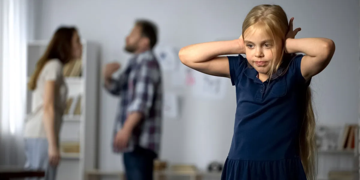 Young girl covering ears while parents argue in the background