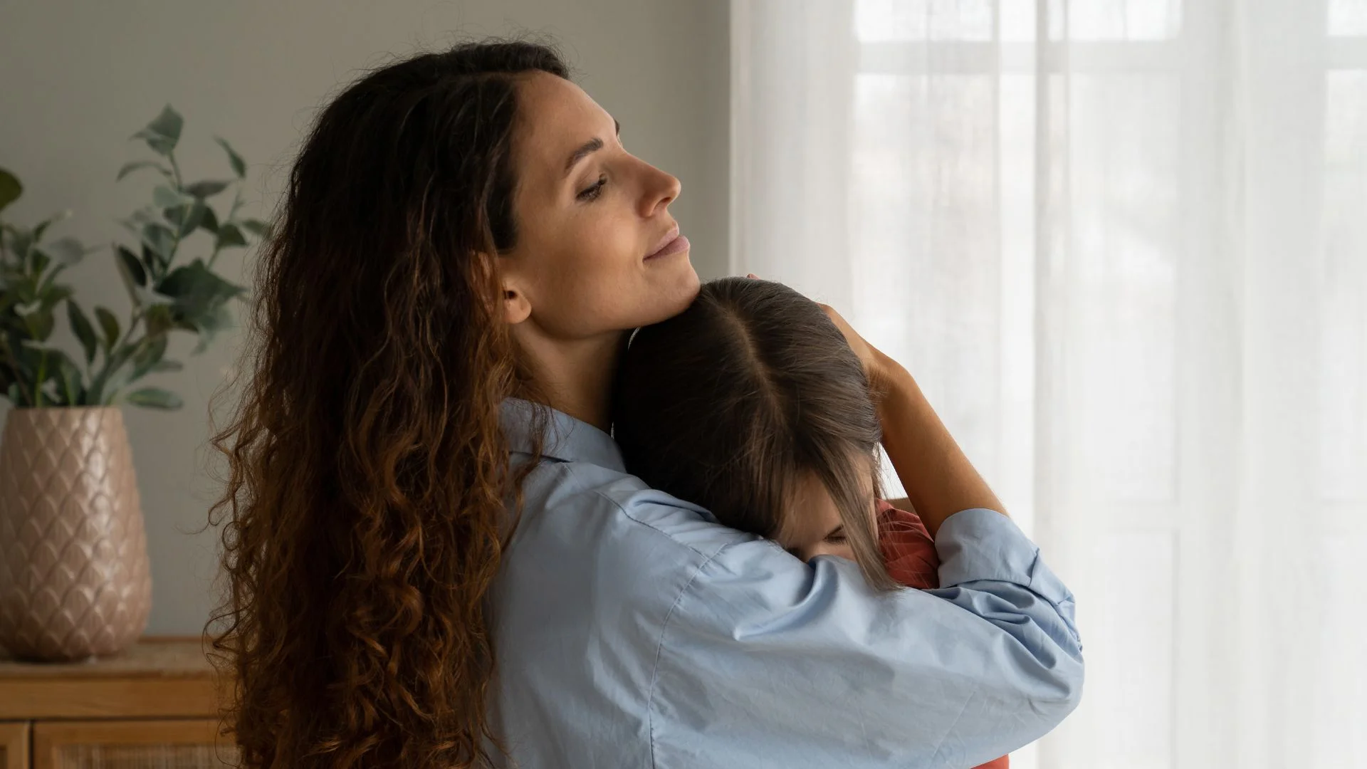 Mother holding her daughter in a warm embrace by a sunlit window